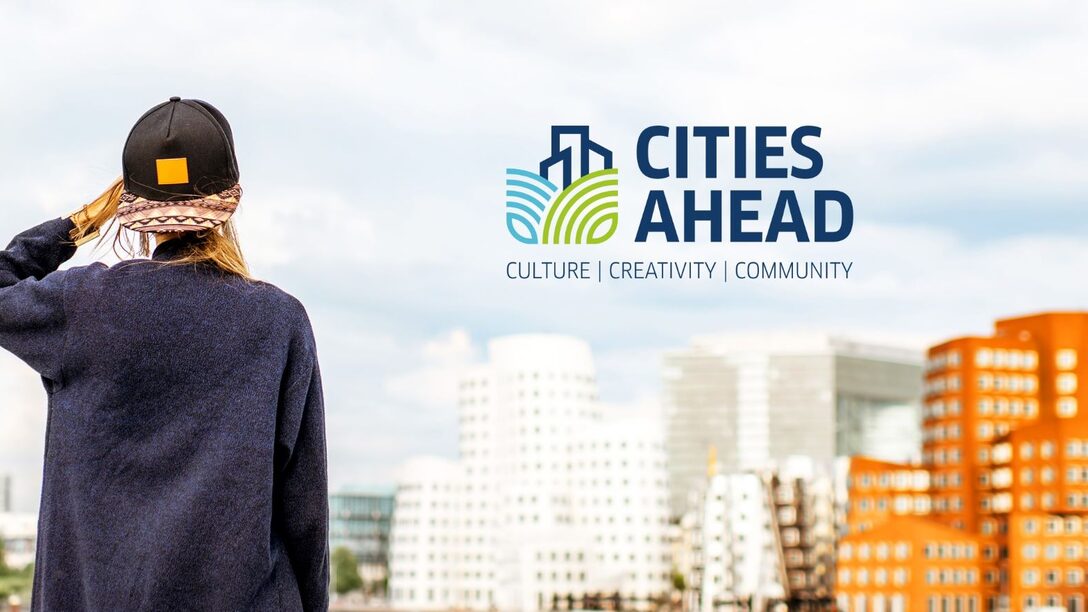 Junge Frau mit Cap von hinten, die auf eine Ansammlung von mehrstöckigen Häusern blickt. Darüber das "Cities Ahrad"-Logo