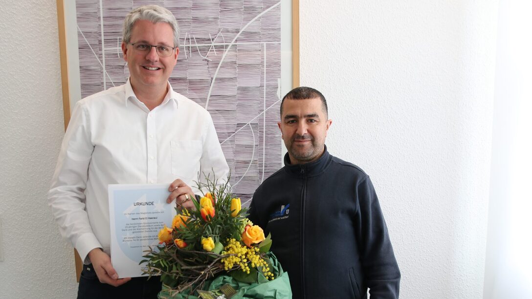 Der Oberbürgermeister zeigt die Urkunde und El Hasnaui hält einen Blumenstrauß in der Hand.