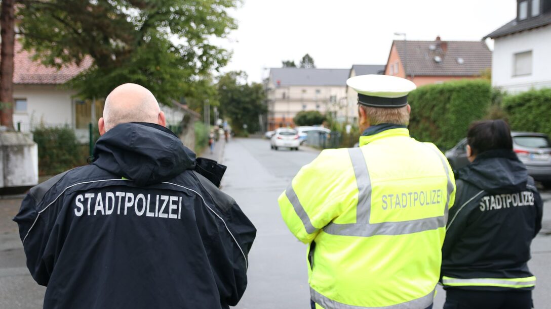 Drei Personen von hinten in Jacken mit der Aufschrift "Stadtpolizei".