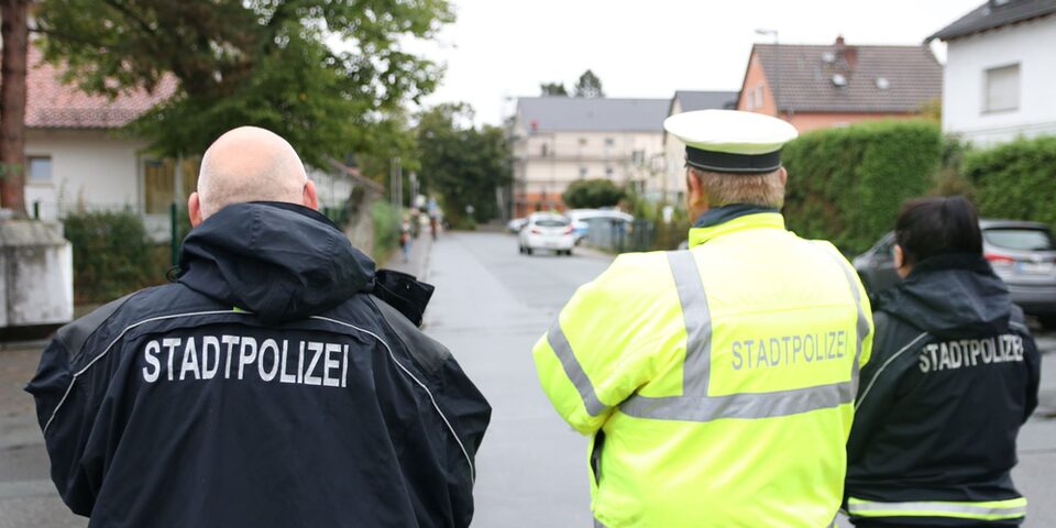 Drei Personen von hinten in Jacken mit der Aufschrift "Stadtpolizei".