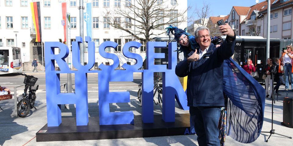 Oberbürgermeister Patrick Burghardt schießt ein Selfie vor dem neu eingeweihten Rüsselsheim-Schriftzug