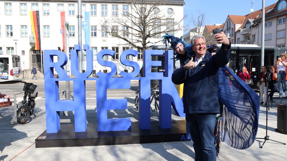 Oberbürgermeister Patrick Burghardt schießt ein Selfie vor dem neu eingeweihten Rüsselsheim-Schriftzug