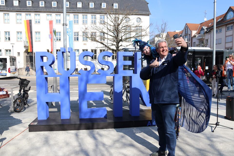 Oberbürgermeister Patrick Burghardt schießt ein Selfie vor dem neu eingeweihten Rüsselsheim-Schriftzug