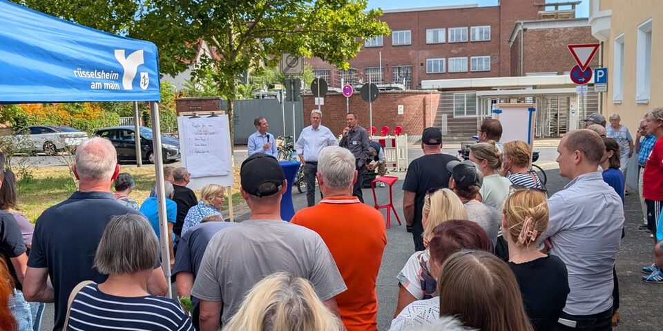 Menschenmenge steht auf der Straße. Im Hintergrund ein "Rüsselsheim am Main"-Pavillion sowie Oberbürgermeister Patrick Burghardt und Stadtrat Simon Valerius.