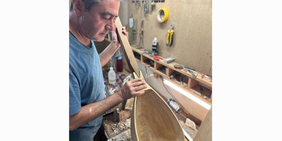 Mann fertigt ein Holz-Instrument. Im Hintergrund eine Werkbank