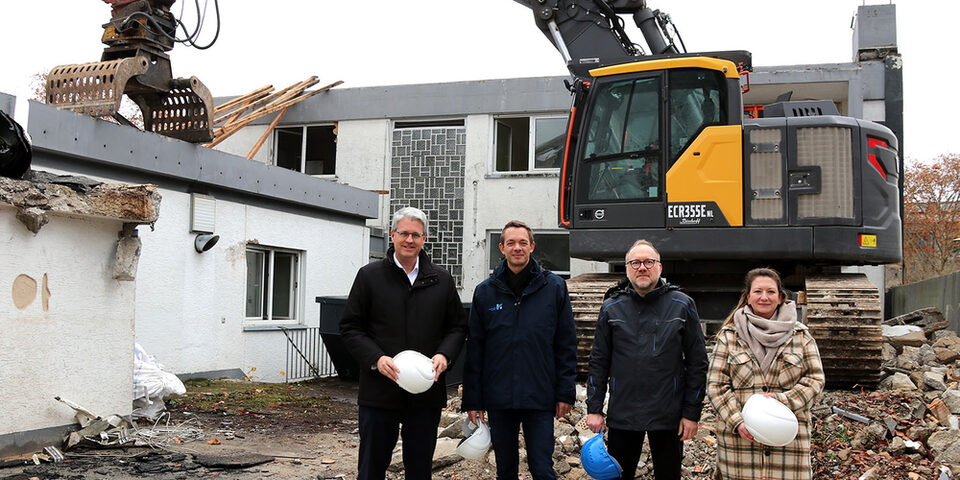 Im Hintergrund ein Bagger und halb abgerissenes Gebäude. Davor stehen: Oberbürgermeister Patrick Burghardt, Stadtrat Simon Valerius, Daniel Langer und Anna Steeg von der Stadtverwaltung.