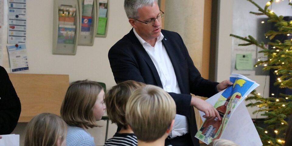 Oberbürgermeister Patrick Burghardt zeigt auf ein gemaltes Bild. Davor stehen Kinder, die man von hinten sieht.
