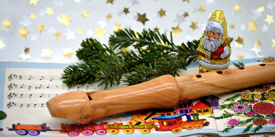 Liederheft mit Noten liegt auf Tischdecke mit Sternen. Darüber ein Tannenzweig, eine Blockflöte und ein Schokoladen-Nikolaus.