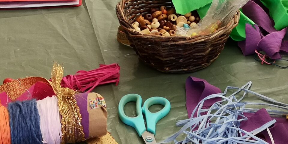Bastelmaterialien wie Schere, Bänder und Perlen liegen auf einem Tisch bereit.