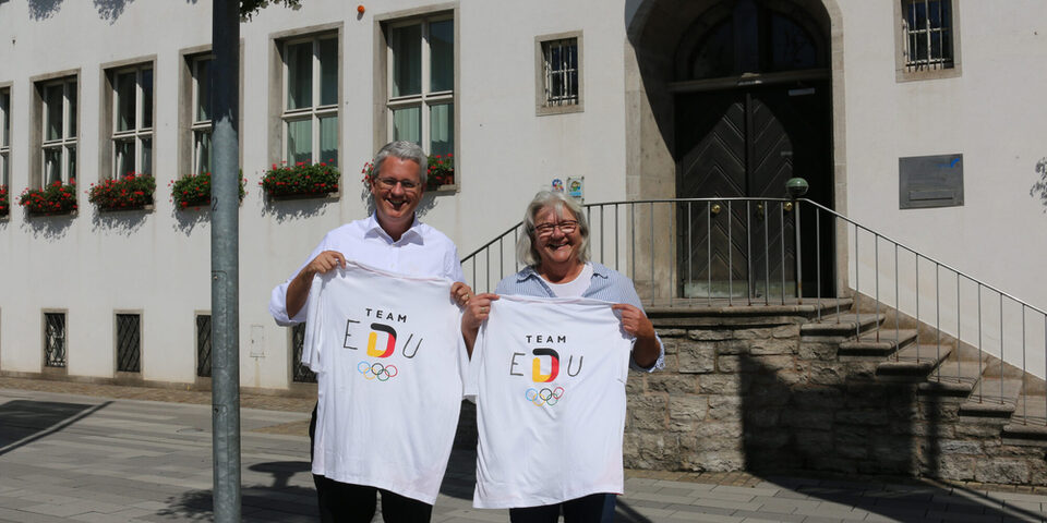 Oberbürgermeister Patrick Burghardt und Anette Tettenborn (Fachbereichsleitung Sport und Ehrenamt) halten "Team EDU"-T-Shirts.