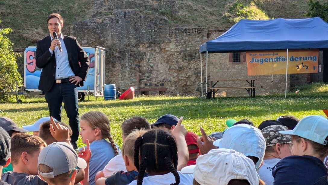 Bürgermeister Dennis Grieser eröffnet die Ferienspiele. Im Vordergrund sind einige Kinder zu sehen.