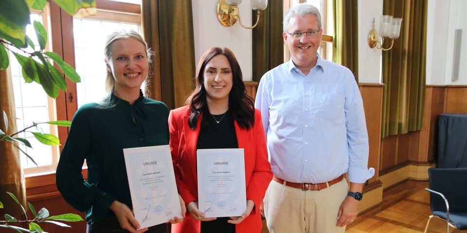 Nadine Hartmann und Justina Rogalski halten ihre Ernennungsurkunden in den Händen, Oberbürgermeister Patrick Burghardt steht daneben