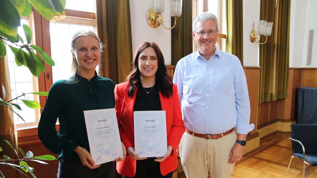 Nadine Hartmann und Justina Rogalski halten ihre Ernennungsurkunden in den Händen, Oberbürgermeister Patrick Burghardt steht daneben