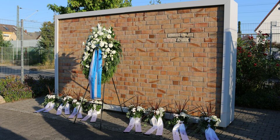 Mahnmal in der Grabenstraße: Mauer und ein großer Kranz mit Schleife sowie kleinere Kränze davor.