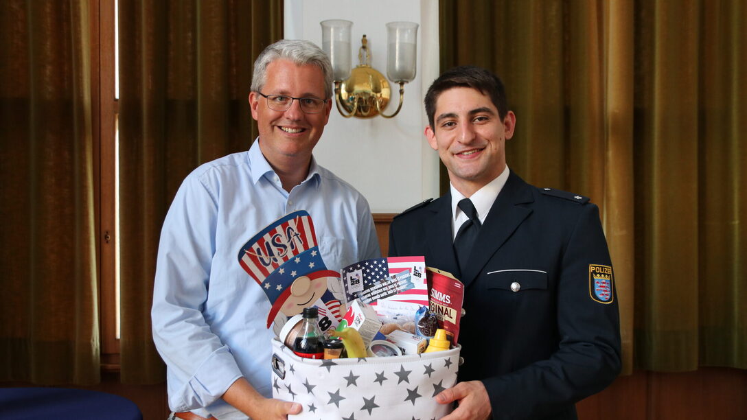 Oberbürgermeister Patrick Burghardt und Eduard Trippel halten einen Geschenkkorb mit Snacks aus den USA