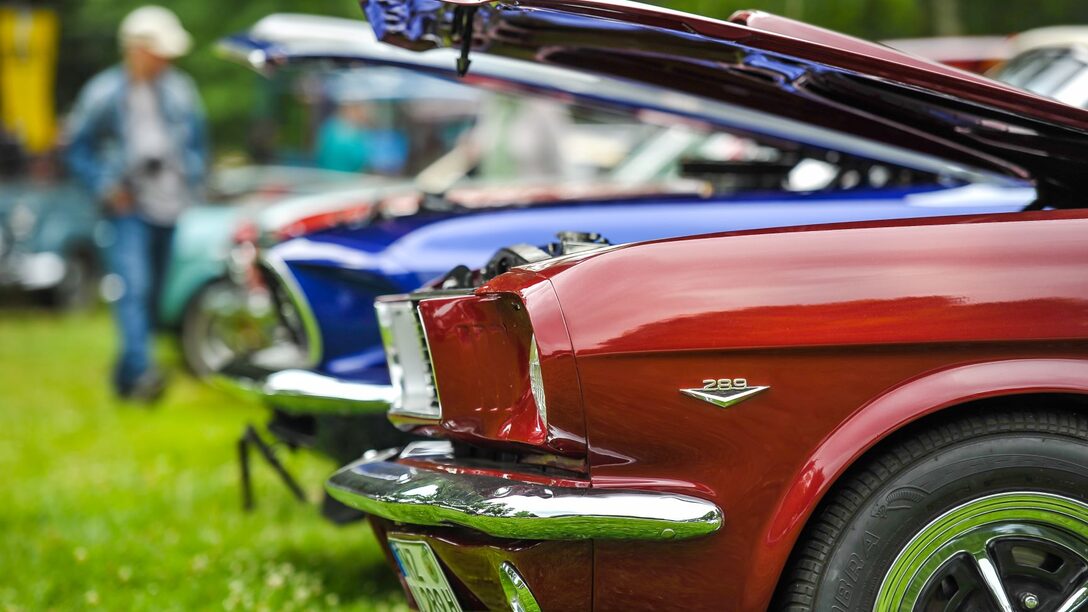 Roter Oldtimer im Vordergrund, weitere im Hintergrund auf Wiese.