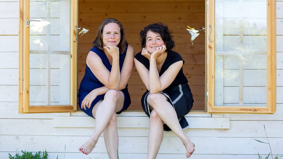 Zwei Frauen sitzen auf dem Fensterbrett eines geöffneten Fensters