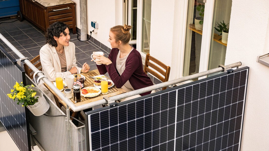 Zwei Frauen frühstücken auf einem Balkon mit Balkonkraftwerk