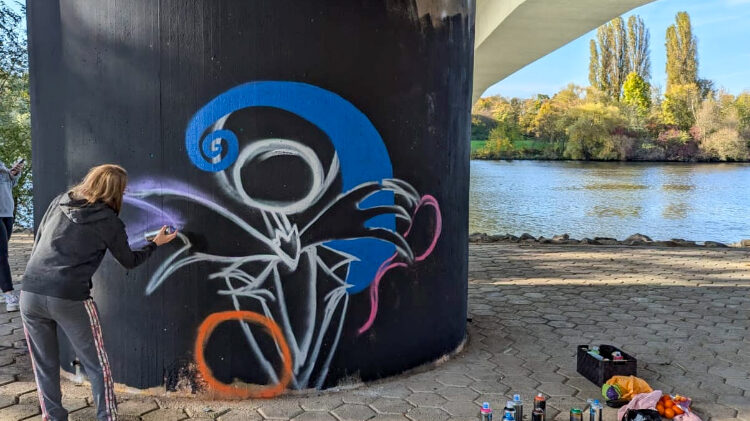 Eine Person sprüht Grafitti auf eine Stele unterhalb der Opelbrücke in Rüsselsheim am Main