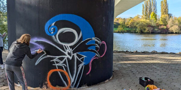 Eine Person sprüht Grafitti auf eine Stele unterhalb der Opelbrücke in Rüsselsheim am Main