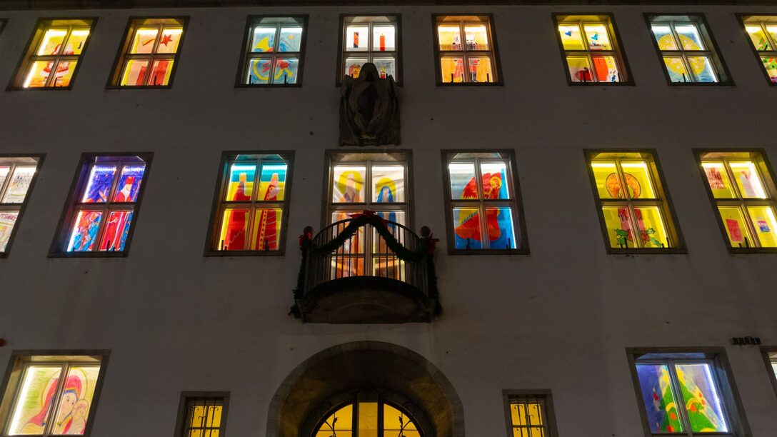 Blick auf die Fassade des Rathauses am Haupteingang. Alle Fenster sind mit weihnachtlichen Bildern erleuchtet.