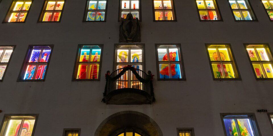 Blick auf die Fassade des Rathauses am Haupteingang. Alle Fenster sind mit weihnachtlichen Bildern erleuchtet.