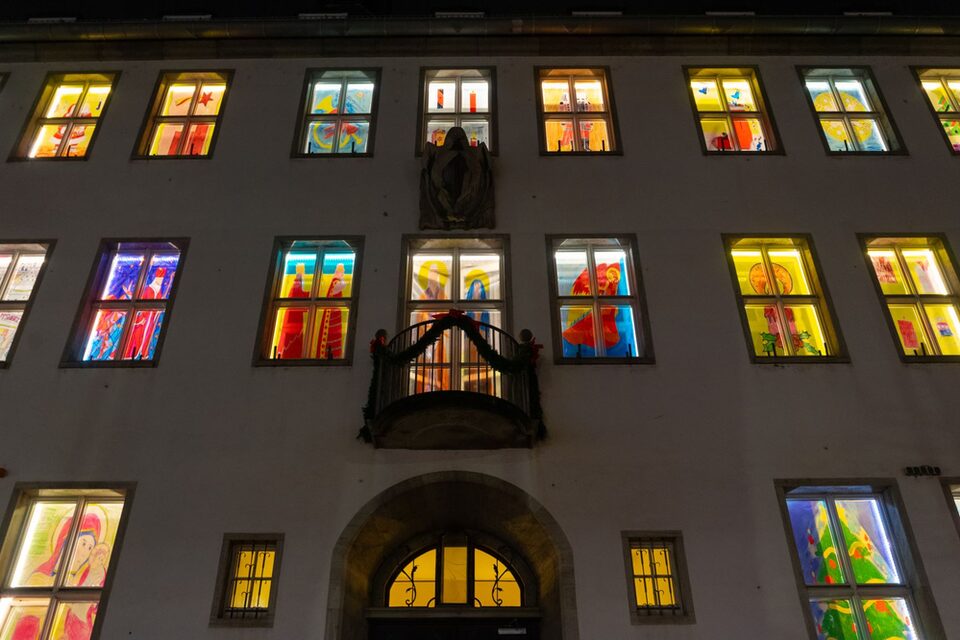 Blick auf die Fassade des Rathauses am Haupteingang. Alle Fenster sind mit weihnachtlichen Bildern erleuchtet.