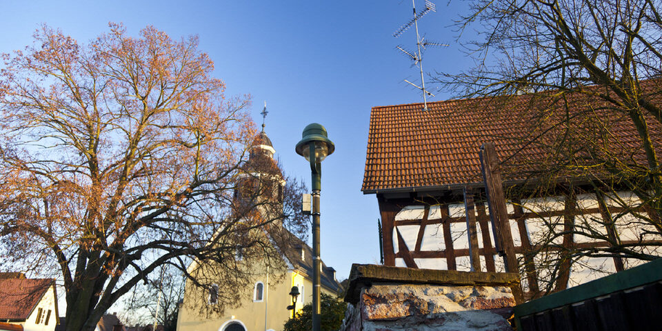 Blick auf den Platz "An der Wied": Im Zentrum die Kirche, daneben eine historische Straßenlaterne und ein Fachwerkhaus.