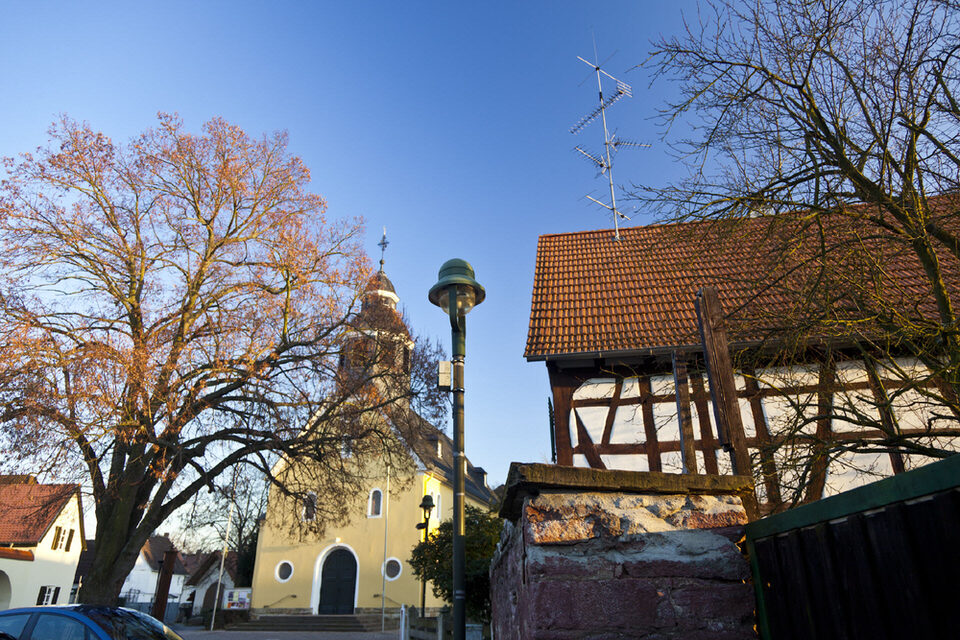 Blick auf den Platz "An der Wied": Im Zentrum die Kirche, daneben eine historische Straßenlaterne und ein Fachwerkhaus.