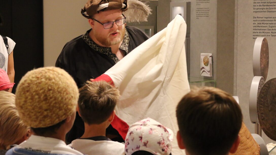 Eine Person zeigt Kindern im Stadt- und Industriemuseum ein Stoffstück.