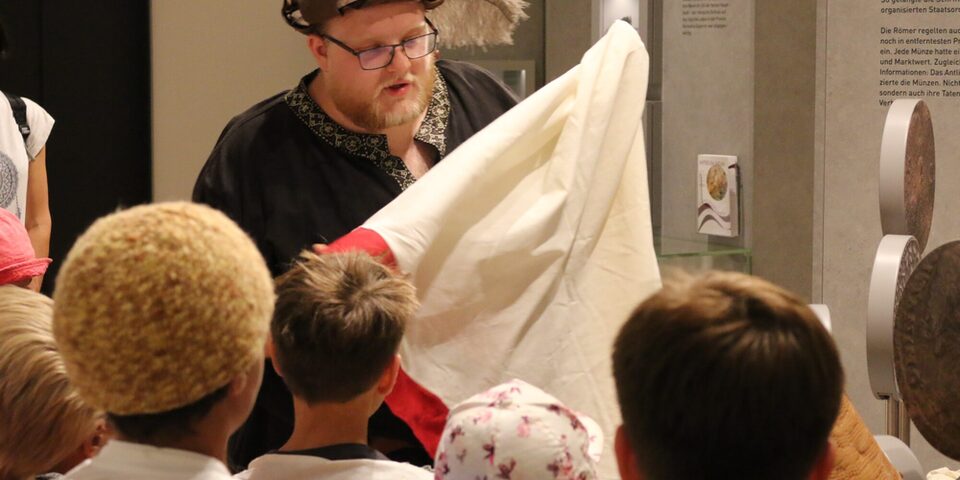 Eine Person zeigt Kindern im Stadt- und Industriemuseum ein Stoffstück.