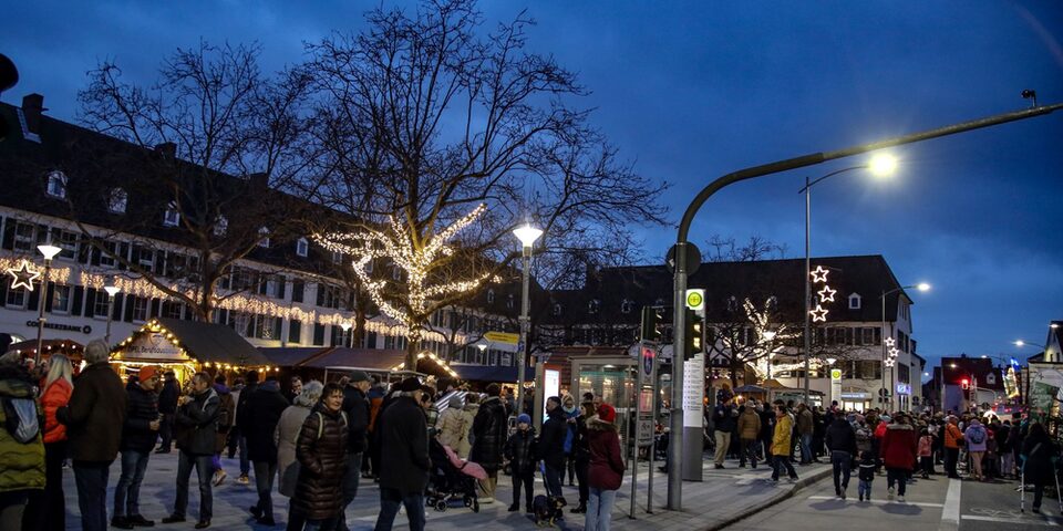 Weihnachtsmarkt auf dem Marktplatz 2023: Blick auf die Frankfurter Straße, auf der sich Menschen tummeln. Im Hintergrund Lichter und geschmückte Buden.