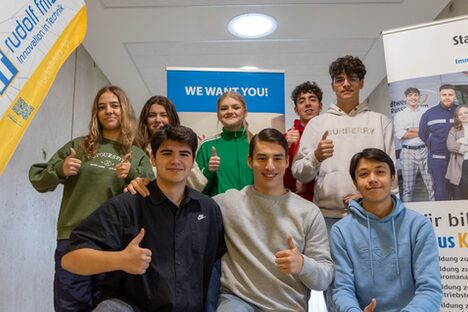 Gruppenfoto der Auszubildenden der Stadtwerke, die alle eine "Daumen hoch"-Geste zeigen. Dahinter Rollups der Stadtwerke und eine Beachflag der Rudolf Fritz GmbH.