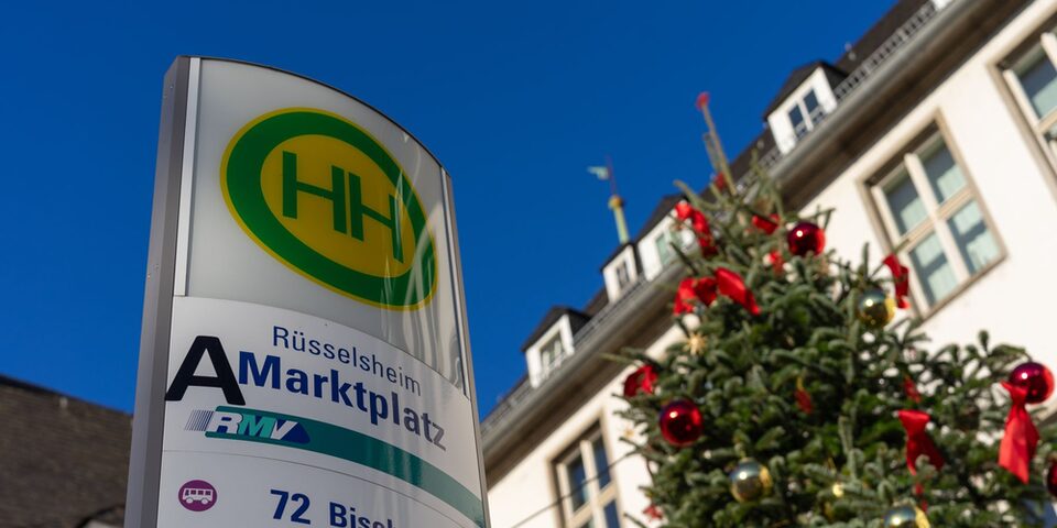 Bushaltestellenschild "Rüsselsheim Marktplatz", daneben ein geschmückter Weihnachtsbaum. Im Hintergrund das Rathaus.