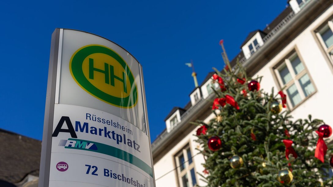 Bushaltestellenschild "Rüsselsheim Marktplatz", daneben ein geschmückter Weihnachtsbaum. Im Hintergrund das Rathaus.