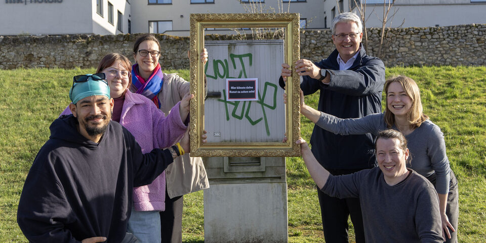 Projektbeteiligte halten einen Bilderrahmen vor einen Stromkasten