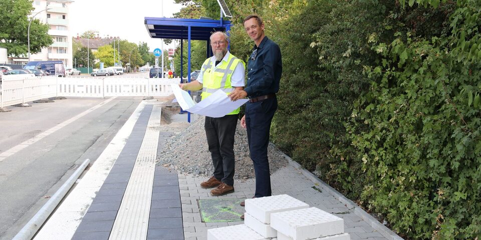 Stadtrat und Abteilungsleiter sehen sich auf der Baustelle für die Haltestelle an der Alexander-von-Humboldt-Schule einen Bauplan an.