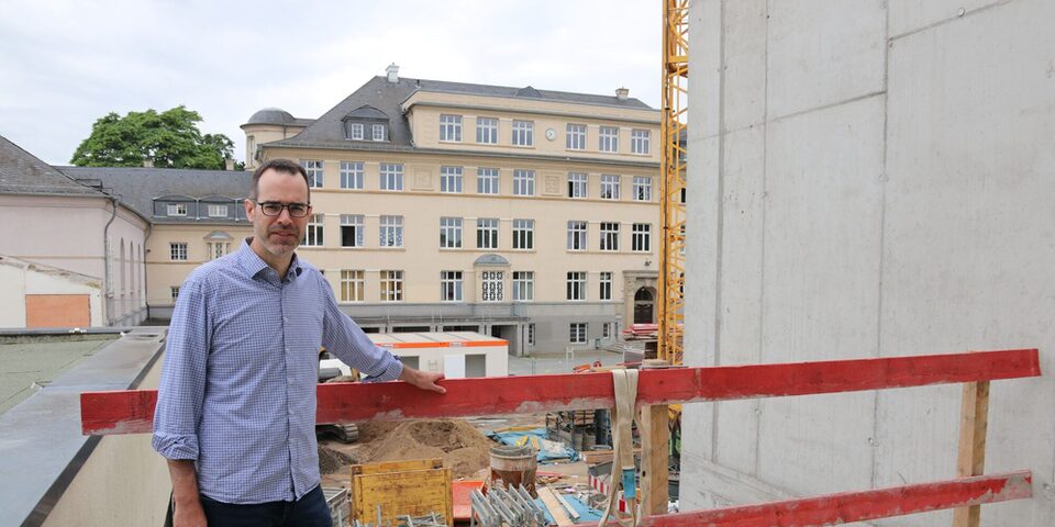 Stadtrat Nils Kraft steht vor der Baustelle Parkschule. Im Hintergrund ist das alte Hauptgebäude zu sehen.