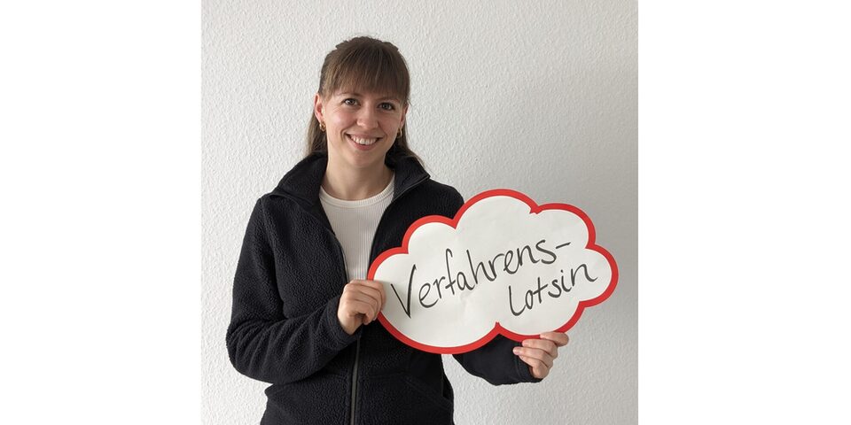 Paulina Volk hält ein Schild, auf dem "Verfahrenslotsin" steht.