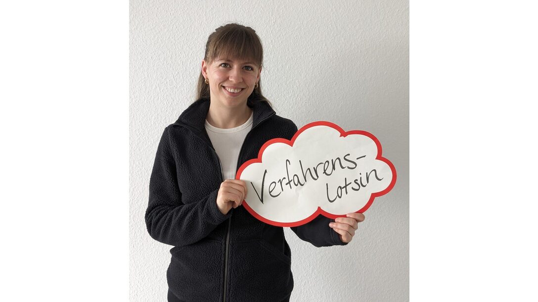 Paulina Volk hält ein Schild, auf dem "Verfahrenslotsin" steht.