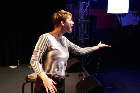 Foto: Hannah Wehrum steht auf einer Bühne, trägt etwas vor und streckt einen Arm aus.
