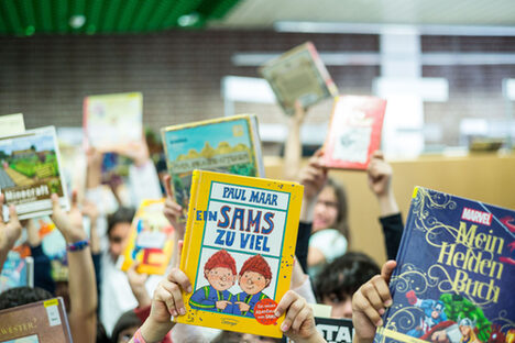 Foto: Hände halten Kinderbücher hoch, im Vordergrund die Bücher "Ein Sams zu viel" und "Mein Heldenbuch"