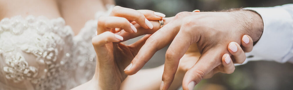 Braut steckt Ring auf die Hand des Bräutigams