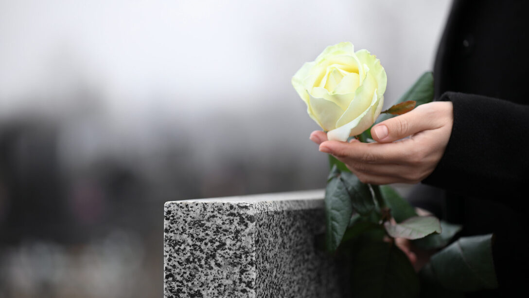 Frau hält weiße Rose in der Nähe eines Grabsteins aus grauem Granit im Freien