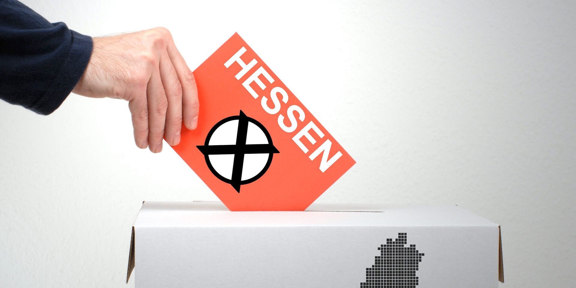 Eine Hand hält eine Karte mit dem angekreuzten Aufdruck "Hessen" über eine Wahlurne