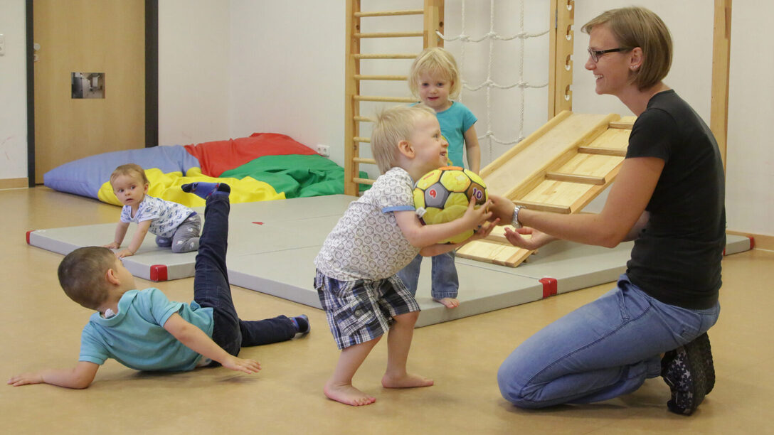 Kleine Kinder turnen und spielen auf Matten mit einer Betreuungsperson