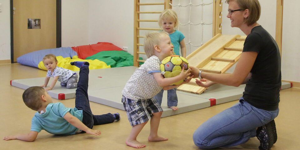 Kleine Kinder turnen und spielen auf Matten mit einer Betreuungsperson