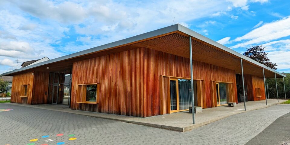 Eingeschossiger Schulbau mit Flachdach und Holzverkleidung, das von großen Fenstern gerahmt wird
