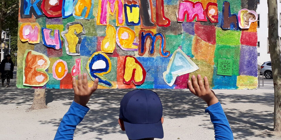 Ein Jugendlicher von hinten und mit Baseball-Kappe hält ein selbstgestaltetes Schild hoch, auf dem zu lesen steht: Kein Müll auf dem Boden