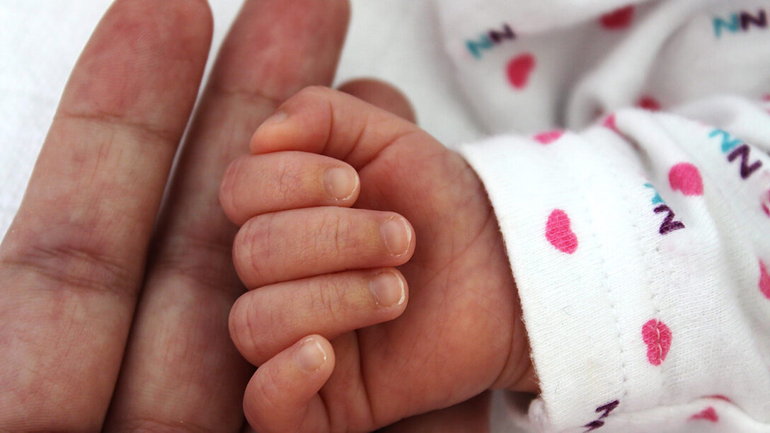 Hand eines Erwachsenen hält Hand eines neugeborenen Babys
